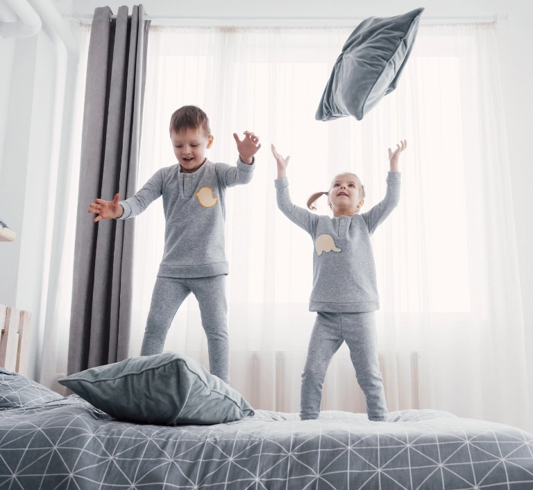 Dzieci bawiące się poduszkami skacząc na łóżku